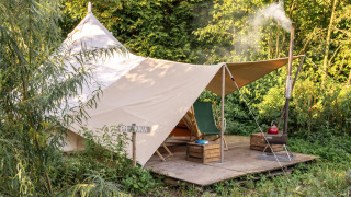 A cozy teepee tent with a canopy and lounge area, surrounded by lush greenery and forest on a wooden platform.