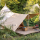 Une tente tipi confortable avec auvent et coin salon, entourée d'une végétation luxuriante en pleine forêt.