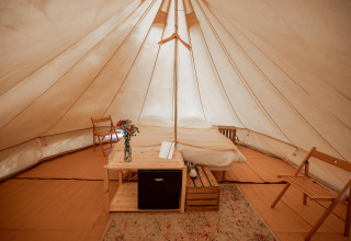 Interior de una confortable tienda tipi con cama doble y sillas en Duo Tipi de RØSTIG, Países Bajos