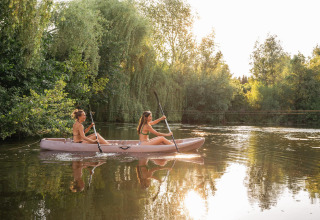 Dos mujeres navegan en kayak por un lago tranquilo rodeado de árboles durante su estancia en glamping.