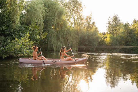 Zwei Frauen paddeln in einem Kajak auf einem ruhigen See inmitten der Natur bei einer Glamping-Unterkunft.
