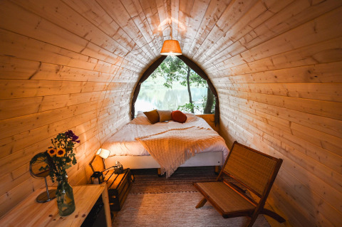 Premium Duo Panorama Pod at RØSTIG in the Netherlands with wooden walls, cozy bed, and lake view.