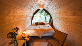 Premium Duo Panorama Pod at RØSTIG in the Netherlands with wooden walls, cozy bed, and lake view.