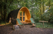 Duo Pod en RØSTIG, Países Bajos: cabaña de madera, dos sillas verdes y una fogata en el bosque.
