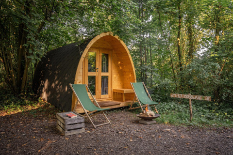 Duo Pod en RØSTIG, Países Bajos: cabaña de madera, dos sillas verdes y una fogata en el bosque.