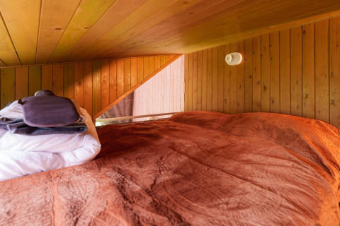 Cozy sleep loft with wood-paneled walls and orange bedding at Luxe & Lazy Lodge, RØSTIG Dorst, Netherlands.