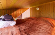 Área para dormir con techo bajo, paredes de madera y ropa de cama roja en Luxe & Lazy Lodge, RØSTIG Dorst.