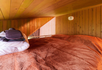 Área para dormir con techo bajo, paredes de madera y ropa de cama roja en Luxe & Lazy Lodge, RØSTIG Dorst.