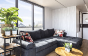 Sala moderna en la casa flotante 'Iere Fügel' con grandes ventanales, sofá gris y plantas, Friesland, Países Bajos.