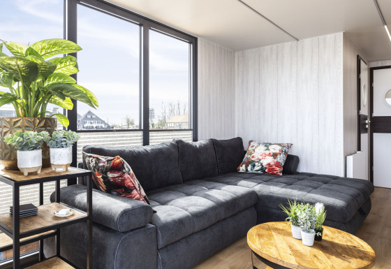 Moderne woonkamer op woonboot 'Iere Fügel', grote ramen, grijze zetel en planten, Friesland, Nederland.