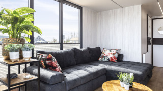 Modern houseboat ‘Iere Fügel’ lounge with large windows, dark sectional sofa and plants, Friesland, Netherlands.