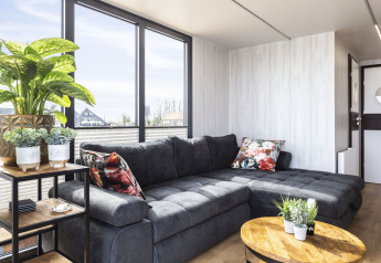 Soggiorno moderno su houseboat 'Iere Fügel' con grandi finestre, divano grigio e piante, Friesland, Paesi Bassi.