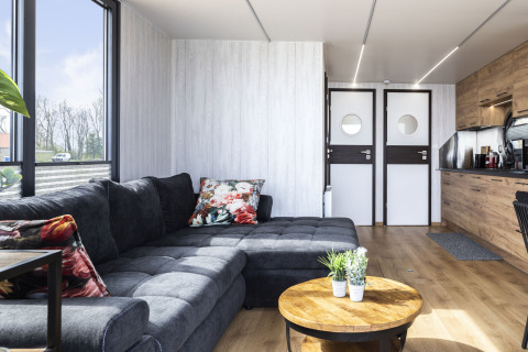 Salón moderno en una casa flotante con sofá gris, cojines florales y cocina en Friesland, Países Bajos.