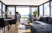 Modern houseboat lounge with large windows, a grey sofa, dining area, and lake view in Friesland.