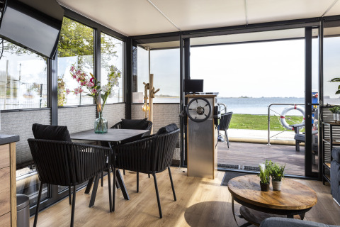 Interior de la casa flotante 'Iere Fügel' en Friesland, con comedor, timón y vistas al lago en los Países Bajos.