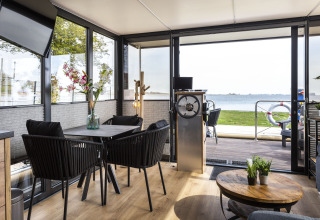 Interior de la casa flotante 'Iere Fügel' en Friesland, con comedor, timón y vistas al lago en los Países Bajos.