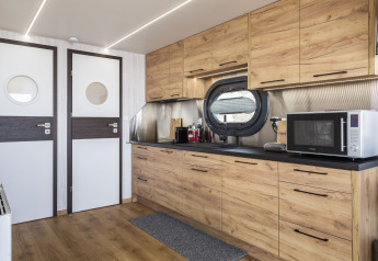 Cocina de casa flotante moderna con gabinetes de madera, ventana redonda, microondas y luces LED en Friesland.