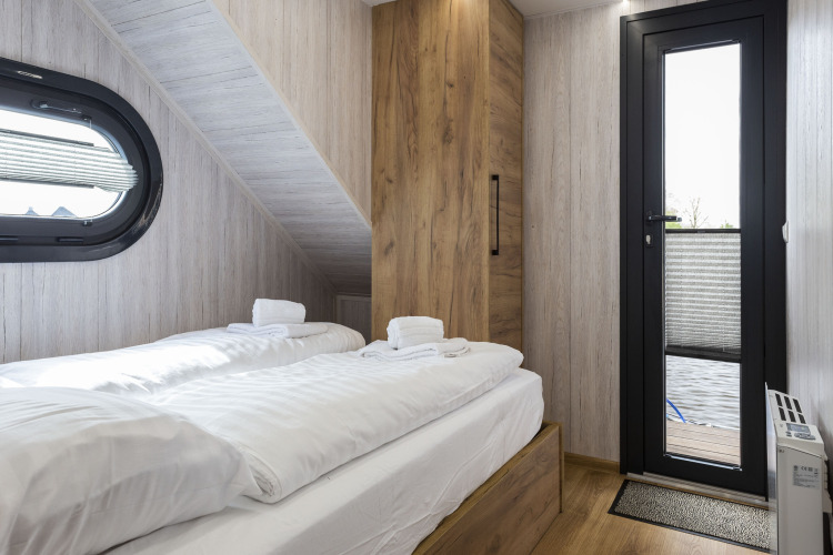 Dormitorio en la casa flotante 'Iere Fügel' con dos camas, armario de madera, ventana y puerta a la terraza en Friesland.