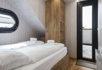 Dormitorio en la casa flotante 'Iere Fügel' con dos camas, armario de madera, ventana y puerta a la terraza en Friesland.