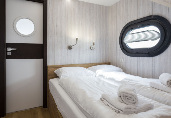 Dormitorio con dos camas individuales y ventana de ojo de buey en Houseboat 'Iere Fügel' en Friesland, Países Bajos.