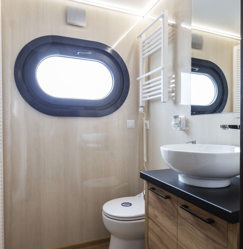 Modernes Hausboot-Badezimmer mit ovalem Fenster, Waschbecken, Holzmöbeln und Spiegel in Friesland.