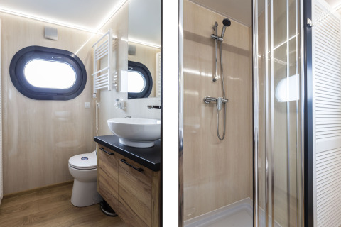 Modernes Badezimmer auf dem Hausboot 'Iere Fügel' mit Bullaugenfenster, Waschbecken, Toilette und Dusche.