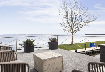 Vista desde Houseboat 'Iere Fügel' en Friesland, Países Bajos, con terraza, lago y árbol al fondo.