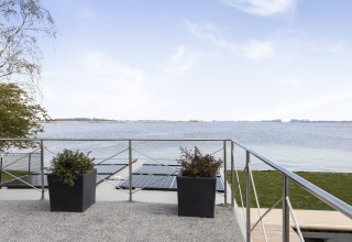 Vista desde la terraza de una casa flotante con paneles solares, macetas y lago en Friesland, Países Bajos