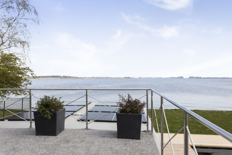 Vue depuis la terrasse d’une péniche avec panneaux solaires, bacs à plantes et lac à Friesland, Pays-Bas