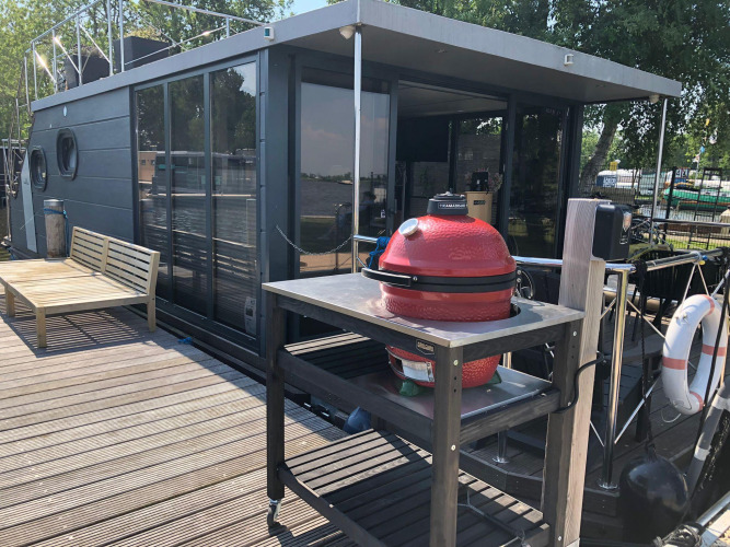 Cubierta de casa flotante con barbacoa roja y banco de madera en Houseboat 'Iere Fügel', Friesland, Países Bajos.