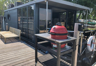 Terrazza di houseboat con barbecue rosso e panchina in legno presso Houseboat 'Iere Fügel', Friesland, Paesi Bassi.