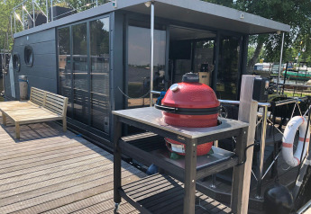 Cubierta de casa flotante con barbacoa roja y banco de madera en Houseboat 'Iere Fügel', Friesland, Países Bajos.