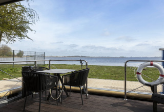 Vista desde el Houseboat 'Iere Fügel' con terraza, mesa, sillas y agua al fondo en Friesland, Países Bajos.
