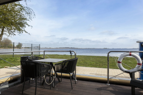 Vista dalla houseboat 'Iere Fügel' con terrazza, tavolo, sedie e vista sull'acqua in Friesland, Olanda.