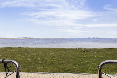 Uitzicht vanaf woonboot over grasveld en meer in Friesland, Nederland, met blauwe lucht en kalm water.