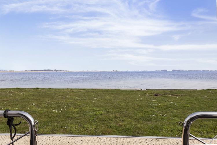 Vue depuis une péniche sur pelouse et lac à Friesland, Pays-Bas, sous un ciel bleu paisible.