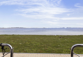 Uitzicht vanaf woonboot over grasveld en meer in Friesland, Nederland, met blauwe lucht en kalm water.