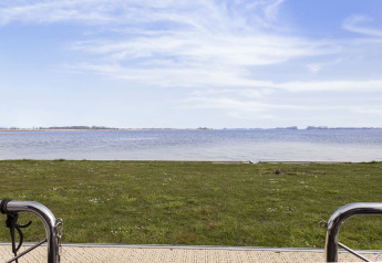 Udsigt fra husbåd over græsplæne og sø i Friesland, Holland, med blå himmel og rolige vand.