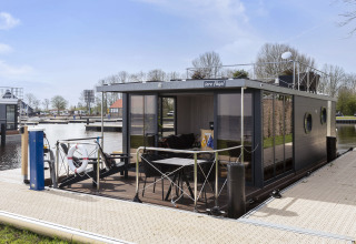 Moderne woonboot 'Iere Fügel' aangemeerd in een jachthaven in Friesland, Nederland, op zonnige dag.