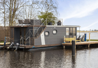 Casa flotante moderna 'Iere Fügel' amarrada en Friesland, Países Bajos, con terraza y vistas al agua.