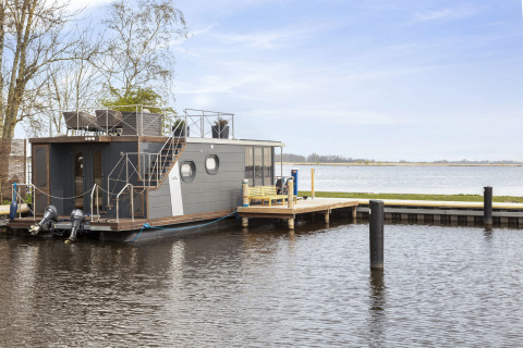 Casa flotante 'Iere Fügel' en Welcome In - Friesland, atracada en un lago tranquilo de los Países Bajos.