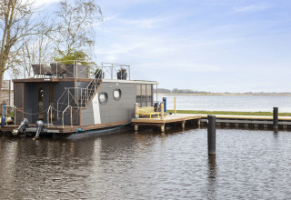 Hausboot 'Iere Fügel' bei Welcome In - Friesland, angedockt an einem ruhigen See in den Niederlanden.