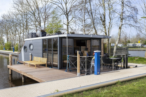 Hausboot 'Iere Fügel' bei Welcome In - Friesland, Niederlande, am Steg mit Terrasse und Sitzbank.
