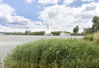 Vista al río con veleros y casa flotante cerca de Houseboat 'Iere Fügel' en Friesland, Países Bajos.