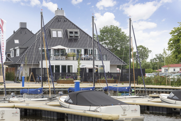 Veleros atracados frente a un moderno houseboat en Friesland, Países Bajos, bajo cielo parcialmente nublado.