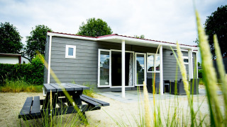 Outside view of a modern Dune Lodge with wooden panels and terrace at Holiday Park Duinhoeve, Netherlands.