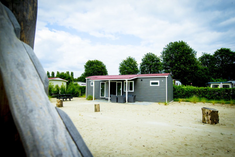 Dune Lodge i Holiday Park Duinhoeve i Holland, omgivet af sand og grønne træer en sommerdag.