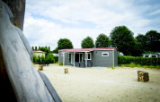 Dune Lodge en Holiday Park Duinhoeve, Países Bajos, rodeado de arena y árboles verdes bajo un cielo nublado.