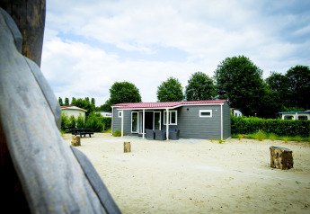 Dune Lodge bij Vakantiepark Duinhoeve in Nederland, met zand, bomen en terrasstoelen op de voorgrond.