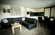 Soggiorno moderno con divano in pelle nera, tavolo da pranzo e cucina nella Dune Lodge, Holiday Park Duinhoeve, Paesi Bassi.